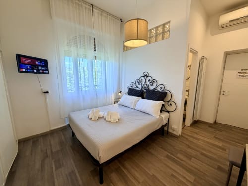 Camera luminosa all'Enjoy Vatican B&B di Roma con letto in ferro battuto, TV a schermo piatto e vista sui monumenti attraverso ampie finestre