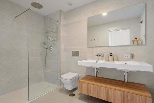 Nowoczesna łazienka w cottagu HomyMarbella w Mijas z prysznicem walk-in, dwoma umywalkami, drewnianą szafką i lustrem ściennym