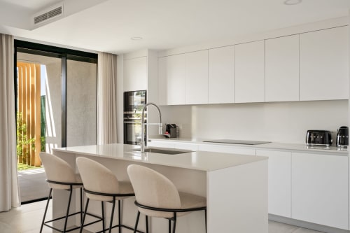 Nowoczesna biała kuchnia z wyspą i miejscami do siedzenia w townhouse HomyMarbella Golf w Miijas, widok na ogród przez przesuwne drzwi
