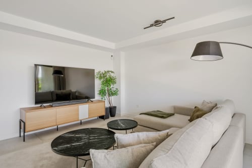 Nowoczesny salon z beżową sofą narożną, drewnianą szafką pod TV i czarnymi stolikami z marmuru w rezydencji HomyMarbella