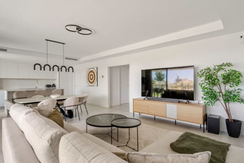 Nowoczesny salon w rezydencji HomyMarbella Mijas z kremową sofą, drewnianym stojakiem na TV i widokiem na ogród