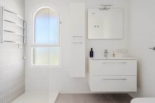 Nowoczesna łazienka w apartamencie w Mijas z białą szafką, lustrem, prysznicem wyłożonym płytkami i łukowatym oknem z widokiem na morze