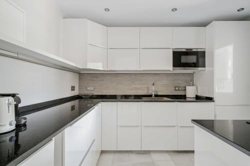 Nowoczesna biała kuchnia z czarnymi blatami granitowymi, stalowymi urządzeniami i wyłożeniem kaflami w apartamencie w Marbelli