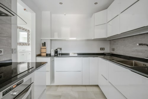 Nowoczesna biała kuchnia z czarnymi blatami granitowymi, stalowymi urządzeniami i wyspą w apartamencie w Mijas