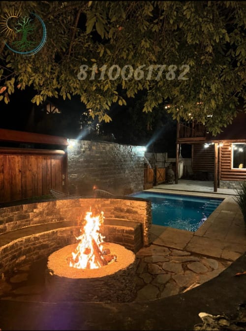 Vista nocturna del jardín trasero del hotel Tierra Cielo & SoLuna con fogata iluminada, piscina resplandeciente y estilo rústico
