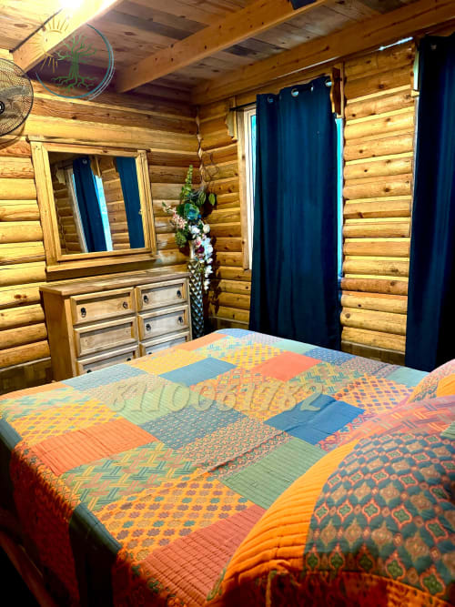 Dormitorio de la cabaña Serrana con colcha patchwork colorida, paredes de troncos, cómoda, espejo y cortinas azul oscuro en Tierra
