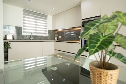 Moderna cocina en villa Gozamena con gabinetes blancos, encimeras oscuras, persianas rayadas y planta verde en maceta