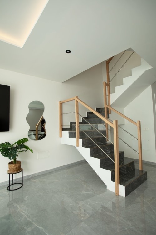 Escalera moderna de villa con barandillas de madera, escalones de mármol negro, paredes blancas y planta en maceta en Gozamena Fuerteventura