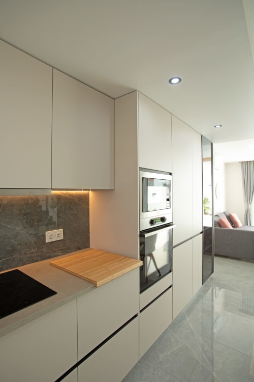 Cocina moderna blanca con encimera de madera, salpicadero oscuro, horno empotrado e iluminación ambiente en villa Gozamena