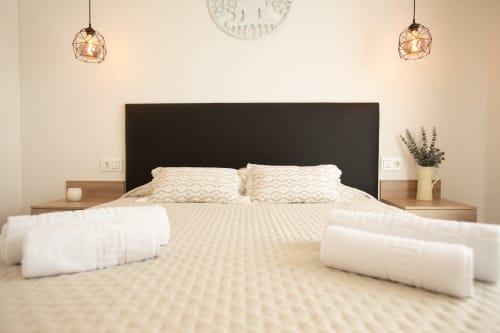 Dormitorio moderno en villa Gozamena con cabecera negra, almohadas de patrón geométrico, lámparas colgantes y mesitas de noche de madera
