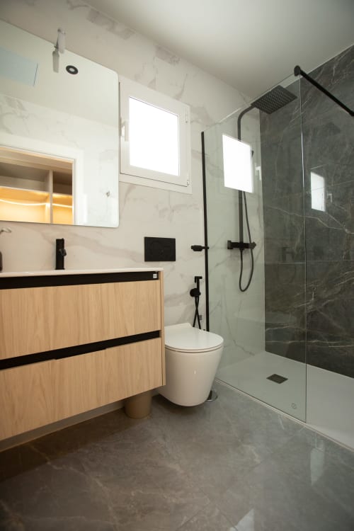Baño moderno en villa Gozamena con tocador de madera, accesorios negros, ducha con cristalería y revestimiento tipo mármol