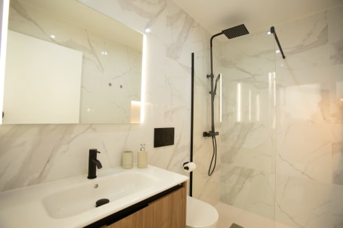 Baño moderno en villa Gozamena con azulejos de mármol, accesorios negros, espejo iluminado y amplia zona de ducha