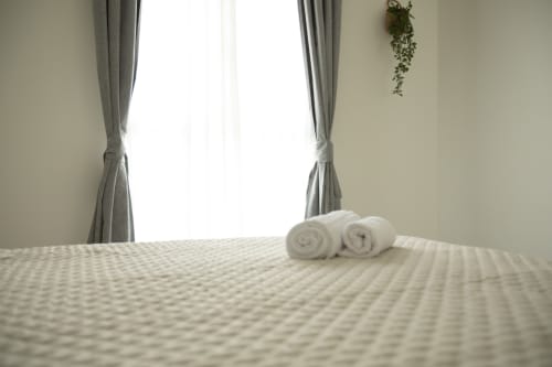 Habitación de lujo en Villa Gozamena con toallas blancas enrolladas en la cama, ventana luminosa con cortinas grises y planta colgante