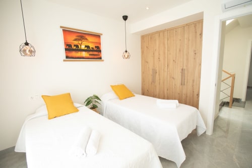 Habitación moderna en villa Gozamena, Fuerteventura: camas gemelas, almohadas amarillas, armario de madera y atardecer africano