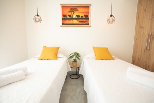 Camas gemelas con almohadas amarillas en Villa Gozamena, Fuerteventura, con lámparas colgantes modernas y arte de atardecer africano