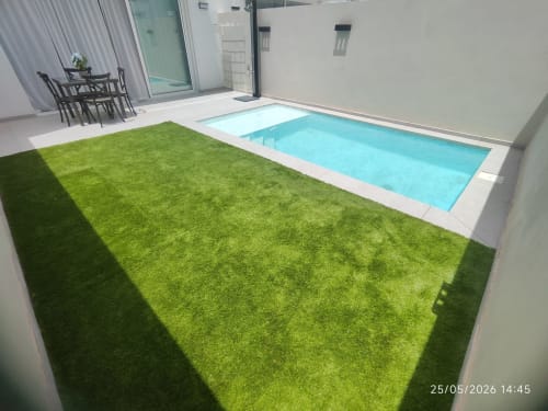 Villa moderna con piscina turquesa brillante, césped cuidado, patio blanco y zona de descanso en Gozamena Fuerteventura