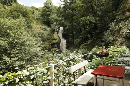Vue sur la cascade depuis la terrasse de La Romanée Sofia à Rosiers-d'Égletons, cadre forestier luxuriant avec table rouge