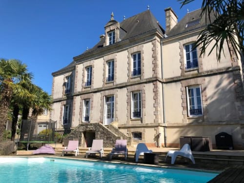 L'hôtel La Pierre Levée à La Gaubretière avec piscine, transats et bâtiment en pierre aux toits mansardés sous ciel bleu