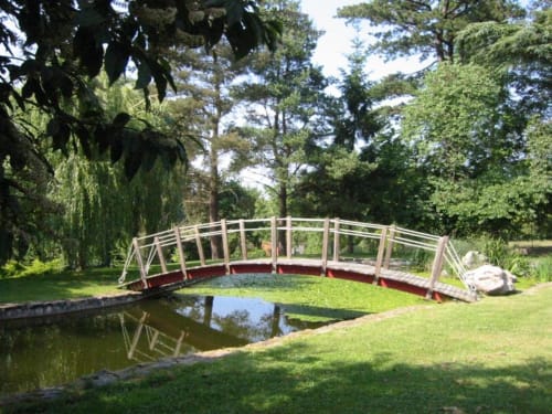 Pont en bois arqué enjambant un étang à l'hôtel La Pierre Levée à La Gaubretière, France, entouré d'arbres et de jardins verdoyants