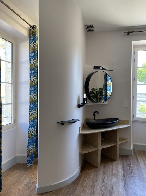Modern bathroom at Le Clos Saint Maurin with black vessel sink, round mirror, wooden vanity, and blue patterned column detail