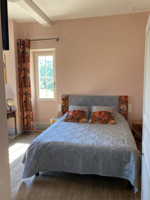 Chambre lumineuse au Clos Saint Maurin avec lit gris, touches florales, murs couleur pêche et vue sur le jardin