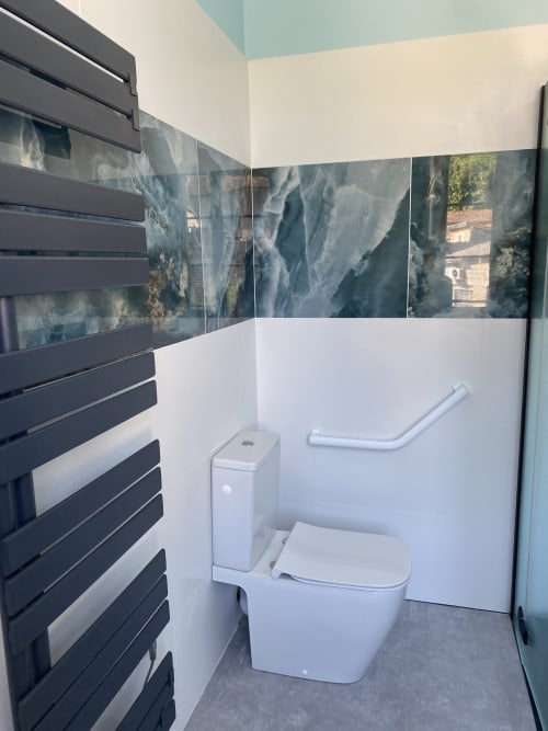 Salle de bain moderne du gîte Le Clos Saint Maurin avec toilettes blanches, radiateur sèche-serviettes noir et carrelage mural imitation cascade