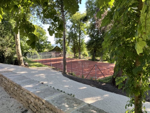 Allée bordée d'arbres menant aux courts de tennis en terre battue rouge du Château de Tharoiseau, un gîte français entouré de forêts.