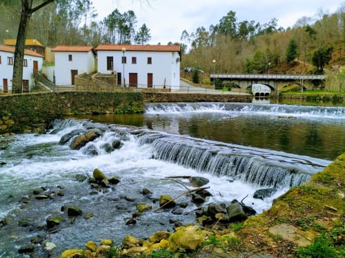 Pink-Shell BnB in Santiago de Riba-UI with waterfall and river, traditional white buildings, stone bridge.