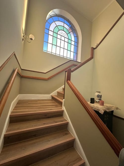 Staircase with wooden steps and handrails at Pink Shell BnB Santiago de Riba-Ui, arched stained glass window above