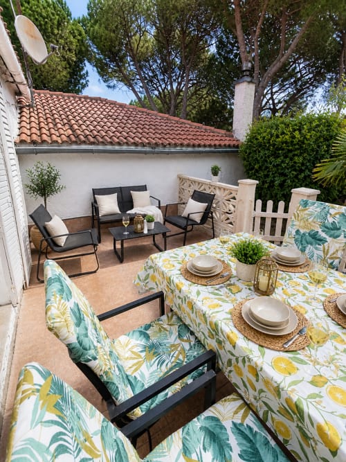 Patio exterior de Las Casitas de Noe en Layos con mesa de comedor, zona de descanso y vistas al frondoso jardín bajo pérgola