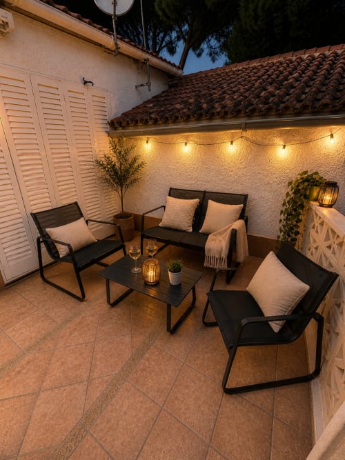 Zona de patio iluminada en Las Casitas de Noe en Layos con muebles negros, guirnaldas de luz y plantas en macetas