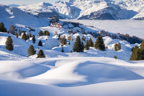 Paysage alpin enneigé à L'Alp'In avec congères ondulantes, forêt et bâtiments de la station de ski de La Plagne