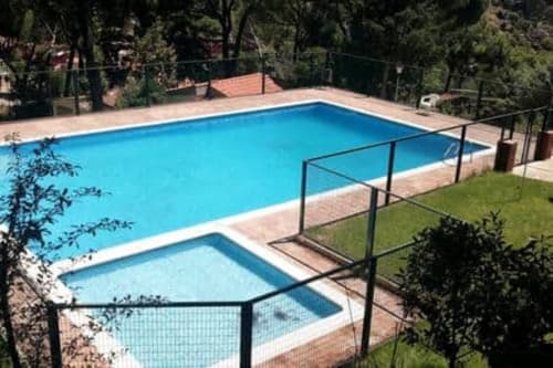 Piscina y jacuzzi con valla de seguridad en Las Casitas de Noe, rodeados de jardines y montaña