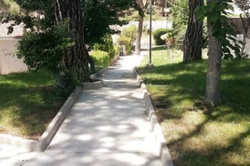Sendero flanqueado por árboles, césped verde y pasarela de hormigón en las Casitas de Noe en Layos