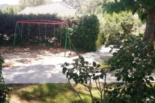 Parque infantil con columpio rojo en la propiedad Las Casitas de Noé en Layos, rodeado de jardines verdes y árboles