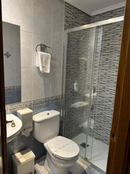 Baño moderno del Hostal Asber Zamora con ducha de cristal, inodoro, lavamanos y paredes alicatadas