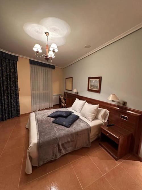 Habitación doble en Hostal Asber de Zamora con cama de madera, suelos de barro y iluminación de araña