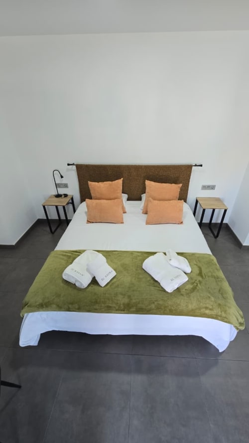 Moderna habitación del Hotel Spa El Batán con cama doble, almohadas naranjas, manta verde, pantuflas blancas y mesillas de noche