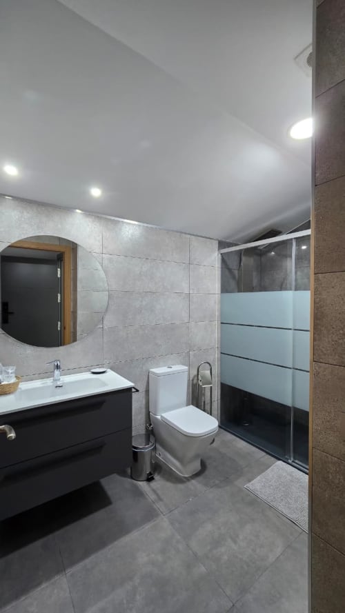 Baño moderno del Hotel Spa El Batán con vanidad negra, inodoro, ducha walk-in con mampara de vidrio y espejo redondo