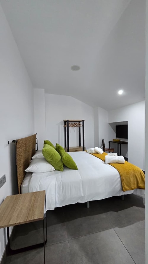 Habitación moderna en El Batán Hotel Spa con cama queen, almohadas verdes, manta amarilla y decoración minimalista blanca en Castillo