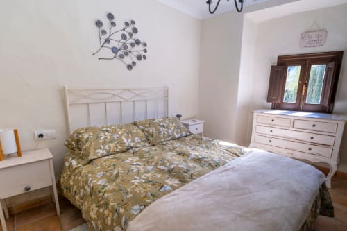 Luminoso dormitorio del Hotel Spa El Batán con cama blanca, ropa de cama floral y muebles crema con vistas al río en Castillo