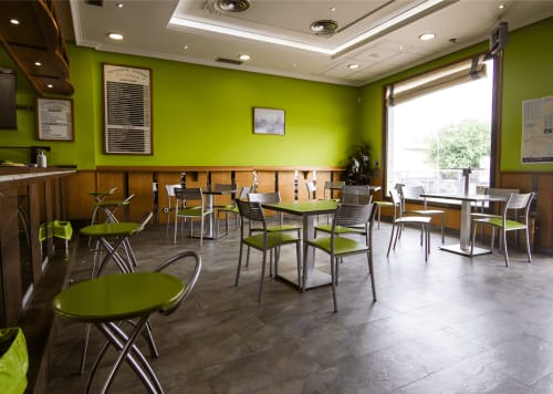Moderno comedor del Hostal El Molino en Collado Villalba con paredes verde lima, paneles de madera y mobiliario contemporáneo.