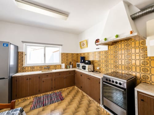 Cozinha Casa Amarela em Lagos com azulejos dourados, armários de madeira, fogão e área de refeições