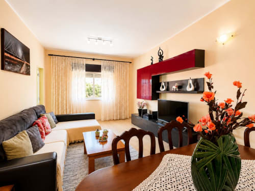 Sala de estar Casa Amarela em Zonas Mágicas, Lagos - assentos confortáveis, TV, prateleiras com destaque vermelho e flores laranja