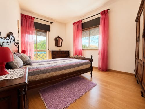 Quarto Casa Amarela em Lagos com cama de madeira escura, cortinas rosa, assoalho de madeira e vistas para o mar