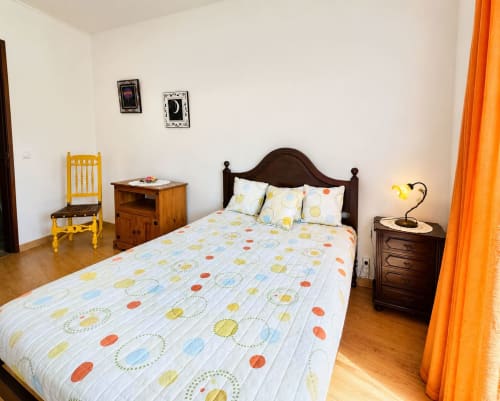 Quarto aconchegante em Casa Amarela, Zonas Mágicas em Lagos com roupas de cama coloridas, móveis de madeira e cortinas laranja
