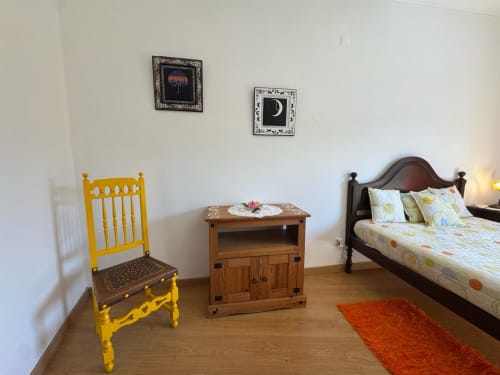 Quarto da Casa Amarela em Lagos com cadeira amarela, criado-mudo em madeira, cama de casal e decoração colorida