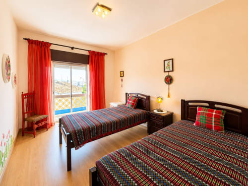 Quarto luminoso na Casa Amarela, Lagos com duas camas, cortinas vermelhas, vista de varanda e decoração tradicional