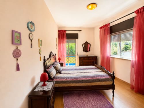 Quarto espaçoso na Casa Amarela em Lagos com cama de madeira, cortinas vermelhas, adornos na parede e vista da cidade