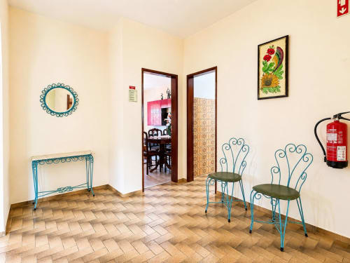 Entrada luminosa da Casa Amarela, Lagos com cadeiras decorativas turquesas, espelho e mesa lateral em piso em espinha de peixe